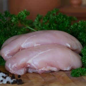 Two chicken breasts on a cutting board with parsley and salt